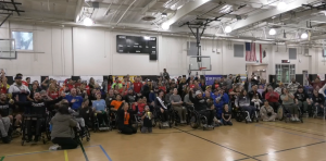 Hundreds of people in wheelchairs pose for a group picture in a high school gym at the Triumph Wheelchair charity event.